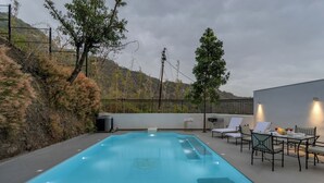 Piscina con vistas a un paisaje montañoso, mobiliario exterior y zona delimitada por una valla.