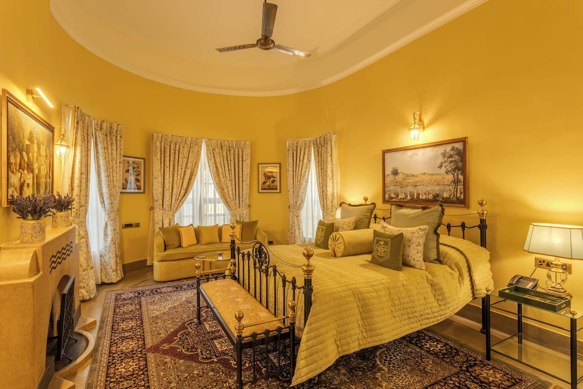 A bedroom with a bed, a sofa, a bench, a desk, and a ceiling fan.