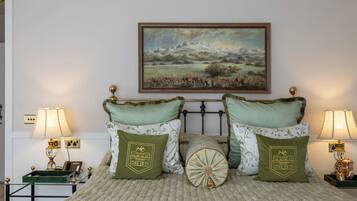 Un dormitorio ordenado con cama, dos almohadas verdes, una almohada decorativa, un cuadro enmarco de un paisaje y lámparas de noche.