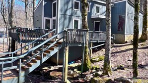 A cabin with a staircase leading to a deck, surrounded by trees.