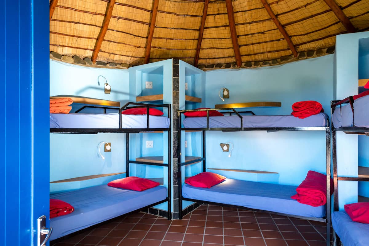 Ein Schlafsaalzimmer mit Etagenbetten, einem Strohdach und blauen Wänden.