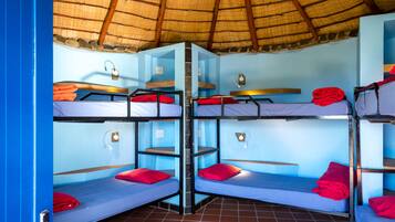 A dormitory room with bunk beds, a thatched roof, and blue walls.
