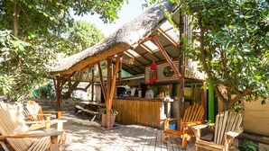 Une terrasse extérieure en bois, dotée d’un toit de chaume, avec des sièges et un espace bar.
