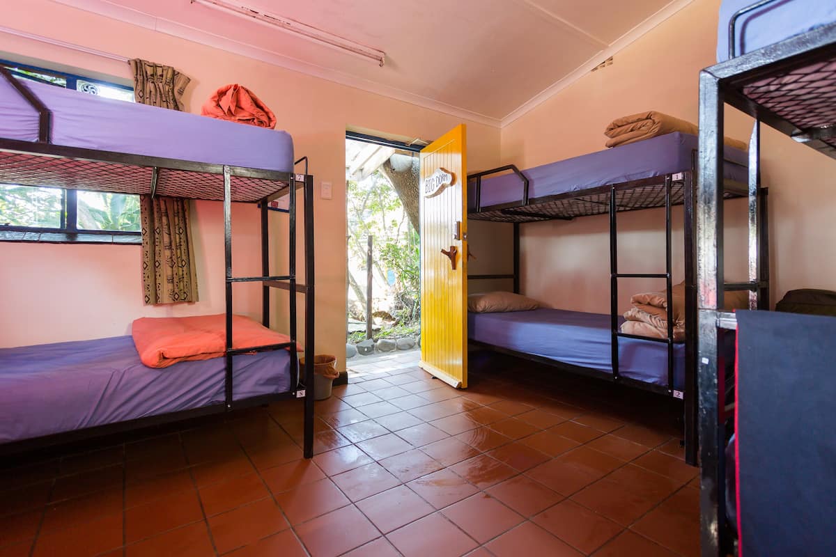 Ein Schlafsaalzimmer mit Etagenbetten, einer Tür und einem Fliesenboden.