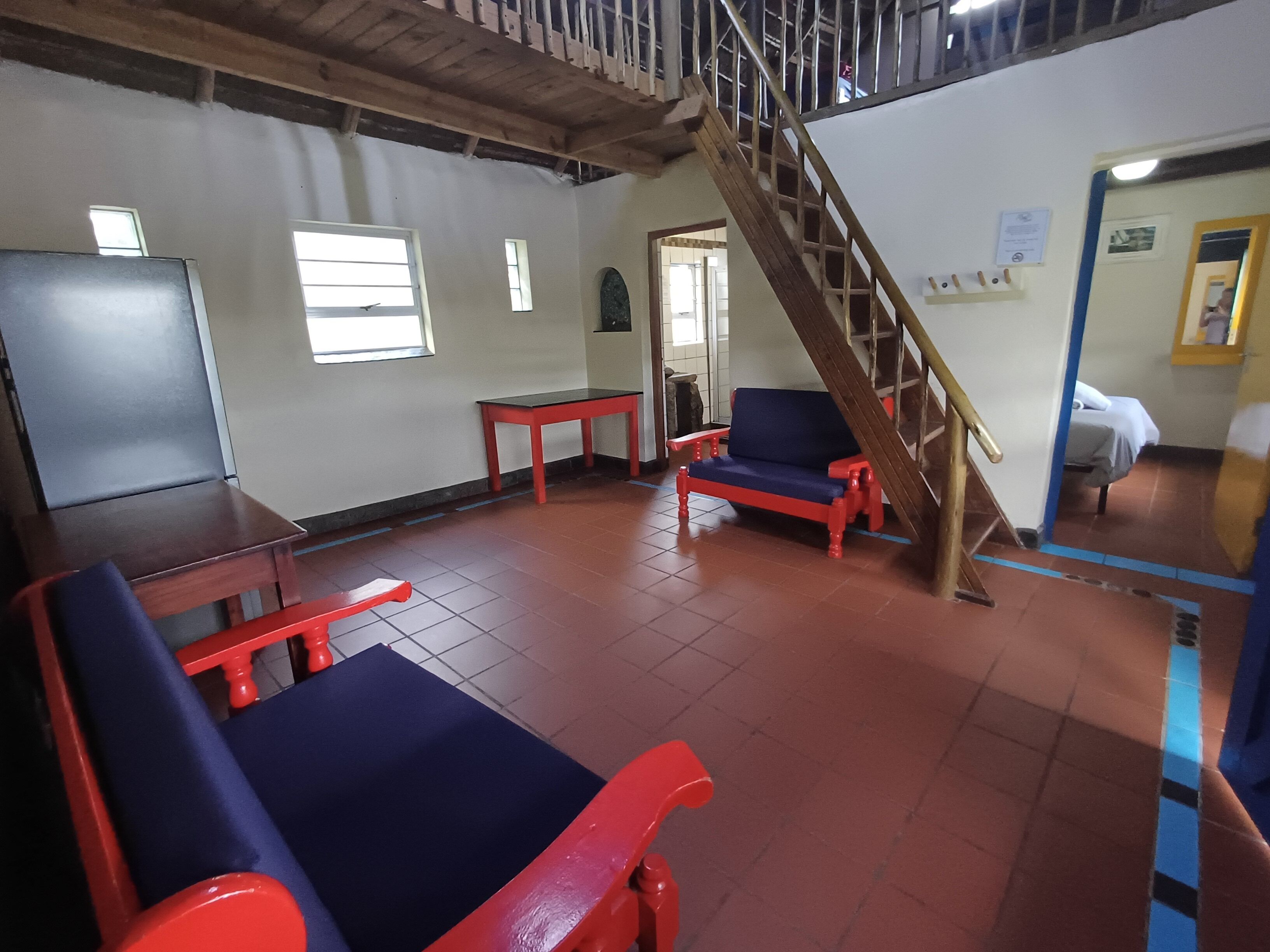 A room with a wooden staircase, a red and blue sofa, a small table, and a whiteboard.