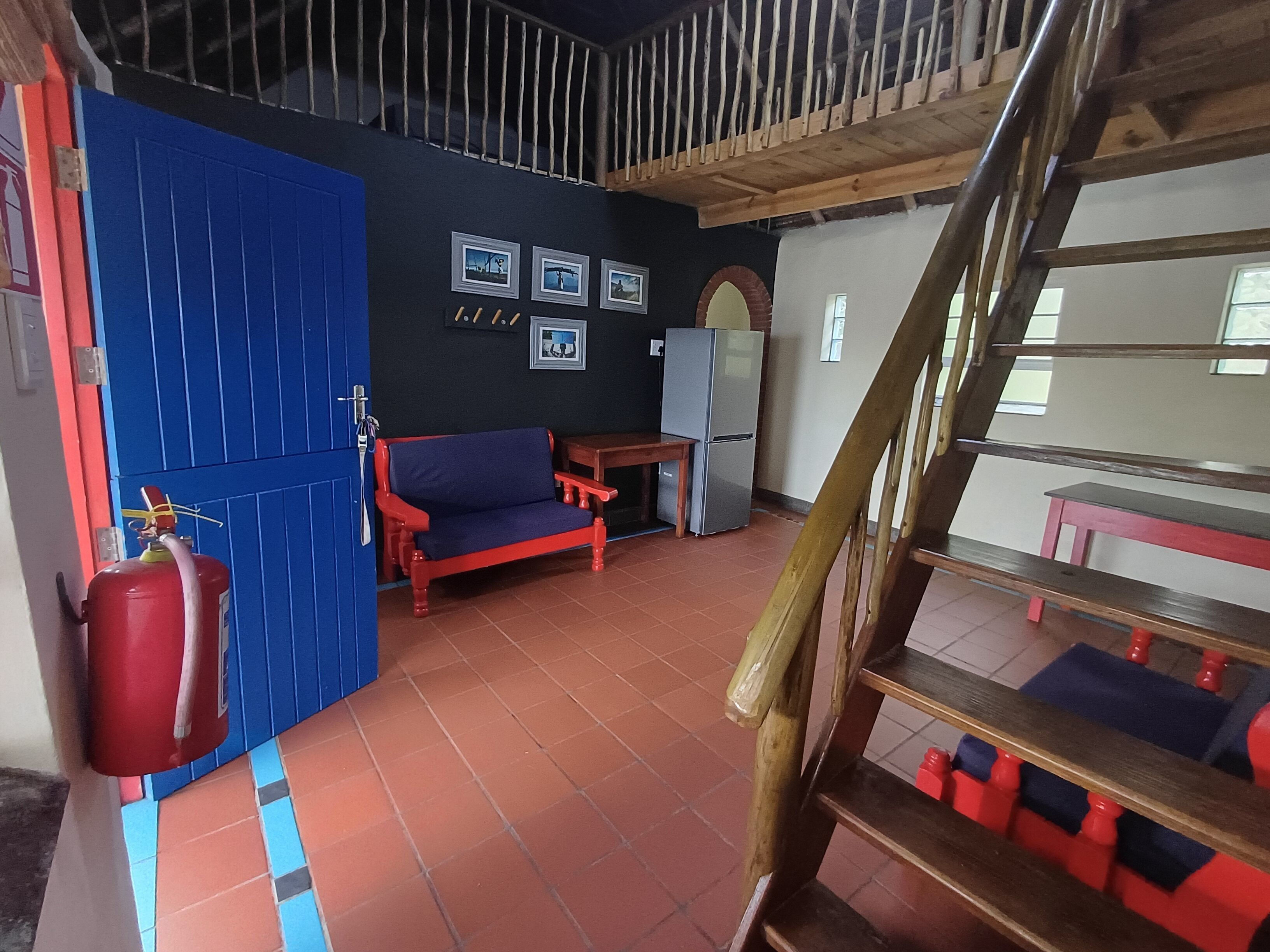 Una habitación con pared azul, sofá rojo, mesa de madera, refrigerador y una escalera.