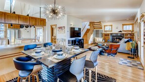 A spacious living area with a dining table set for six, a staircase, and a cozy seating area with a fireplace. - Brilliant Posh Home - Backs to Poudre River Trail (Fort Collins)