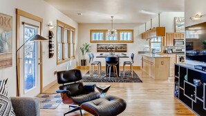 A spacious kitchen with modern appliances, a dining area with a chandelier, and a living room with leather chairs. - Brilliant Posh Home - Backs to Poudre River Trail (Fort Collins)