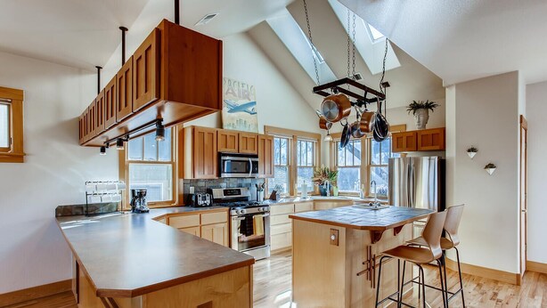 A modern kitchen with wooden cabinets, a central island, and a skylight. - Brilliant Posh Home - Backs to Poudre River Trail (Fort Collins)