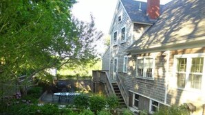 Une maison à deux étages avec un jardin devant, un petit patio et un escalier menant à l’étage supérieur.