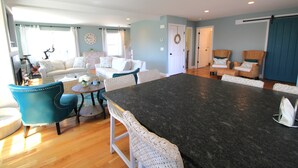 A spacious living room with a large dark grey table, white wicker chairs, and a white sofa. - Beautiful Great Island Ocean Club Home (2368) (Yarmouth)