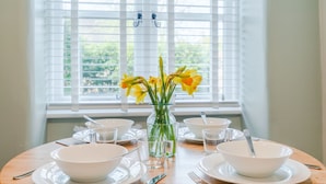 A dining table set with white plates, bowls, and clear glasses, with a vase of yellow flowers in the center. - Gable Cottage  - Dog Friendly, Meysey Hampton near Cirencester (Meysey Hampton)