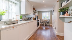 A modern kitchen with white cabinetry, a built-in oven, and a dining area with a table and chairs. - Gable Cottage  - Dog Friendly, Meysey Hampton near Cirencester (Meysey Hampton)