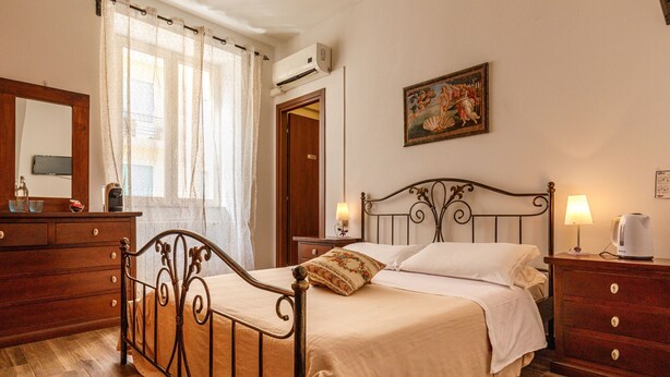 A bedroom with a wooden bed, a nightstand with a lamp, a dresser, a mirror, and a painting on the wall. - Onlyrooms I - Central camp; Secure Area (Cagliari)