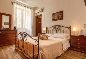 A bedroom with a wooden bed, a nightstand with a lamp, a dresser, a mirror, and a painting on the wall. - Onlyrooms I - Central camp; Secure Area (Cagliari)