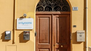 A wooden double door with a decorative metal arch above it, a sign for 'onlyrooms' advertising room bookings, and a utility box on the wall. - Onlyrooms I - Central camp; Secure Area (Cagliari)