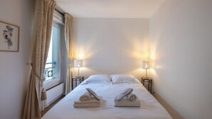 A hotel room with a bed, two bedside lamps, a window with curtains, and a framed picture on the wall. - A little sun in Paris with balconies, 15 minutes from Porte de Versailles (Paris)