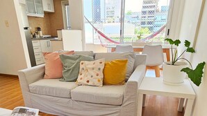 A living room with a sofa, a dining table, and a potted plant. - Cozy Aparment with Balcony, Hammock & Washing Machine (Buenos Aires)