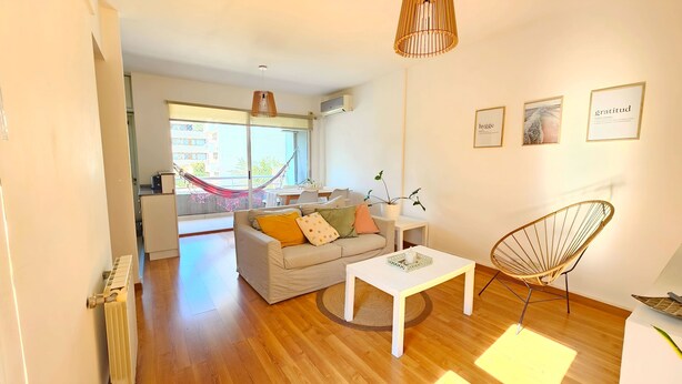 A modern living room with a sofa, coffee table, and a chair. There is a hammock in the background, a dining area, and a kitchen. - Cozy Aparment with Balcony, Hammock & Washing Machine (Buenos Aires)