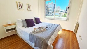 A bedroom with a bed, a nightstand, a window with a city view, and two framed pictures on the wall. - Cozy Aparment with Balcony, Hammock & Washing Machine (Buenos Aires)