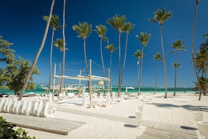 A beach with palm trees, lounge chairs, and a wooden deck.