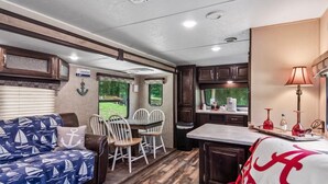 A compact RV interior with a dining area, kitchenette, and a sofa with a nautical theme. - Holiday Haven has Water Access with Private Boat Launch on Lake Guntersville! (Scottsboro)