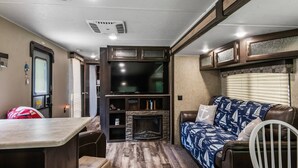 A cozy RV interior with a seating area, a fireplace, a TV, and a dining table. - Holiday Haven has Water Access with Private Boat Launch on Lake Guntersville! (Scottsboro)