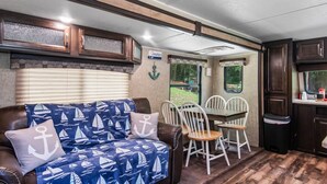 A cozy RV interior with a sofa, dining table, and chairs, a kitchen area, and a view of the outdoors. - Holiday Haven has Water Access with Private Boat Launch on Lake Guntersville! (Scottsboro)