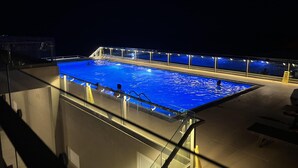 En swimmingpool med en glasvägg och belysning, omgiven av ett trädäck.