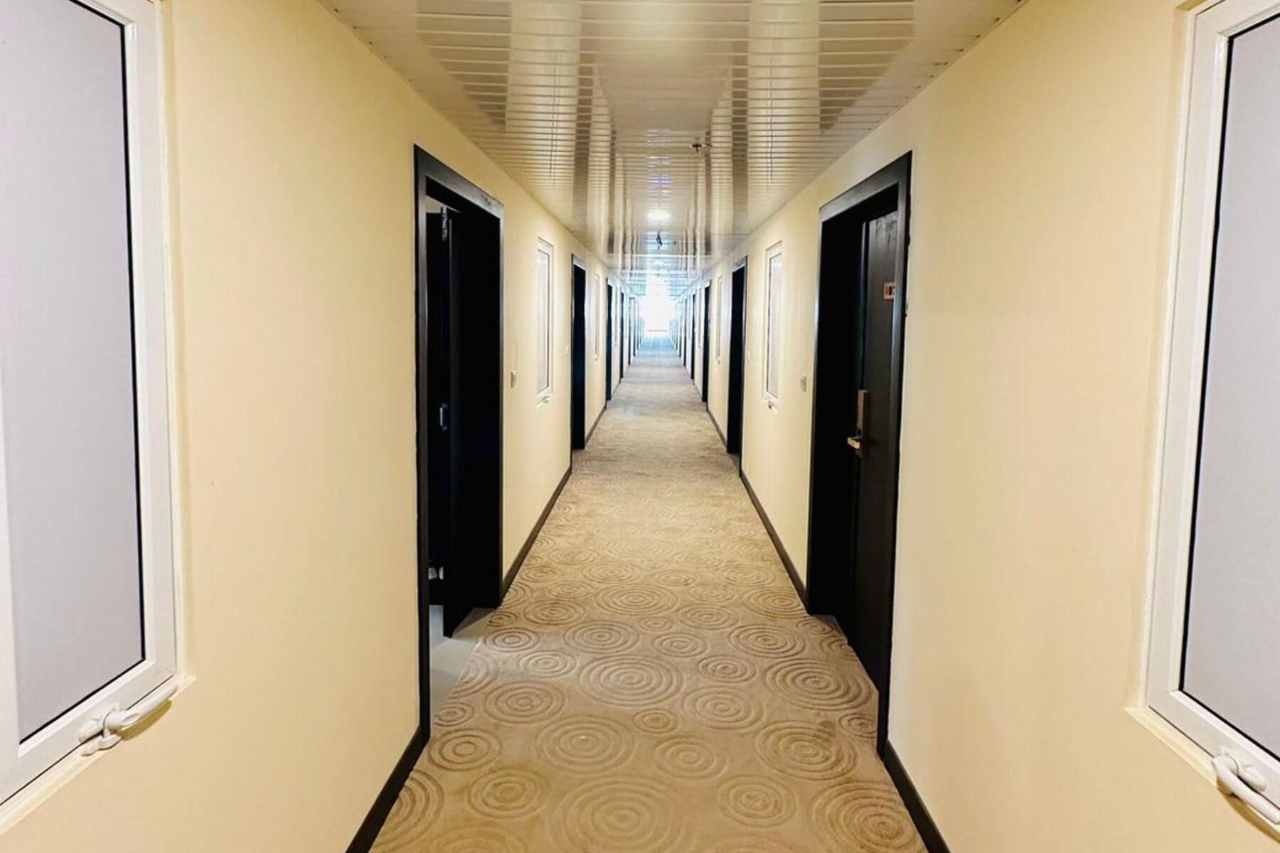 Un pasillo de hotel con alfombra estampada, paredes color crema y puertas negras.
