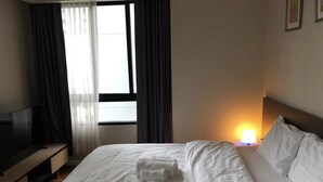 Een hotelkamer met een bed, een tv op een standaard, een nachtkastje met een lamp en een raam met gordijnen.