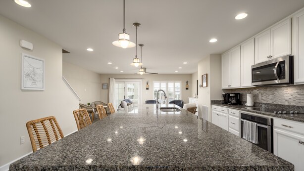 A modern kitchen with a large granite island, white cabinetry, and stainless steel appliances. - New to the Vacation Market! Unit 2B Canal Place (Lewes)