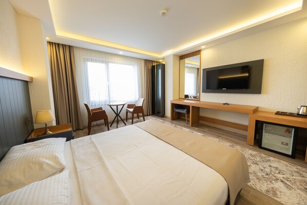 Habitación de hotel con una cama grande, un escritorio, una silla, un televisor y un minibar.
