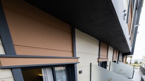 An outdoor seating area with a glass partition, a bed visible through the partition, and a sign with the hotel's name.