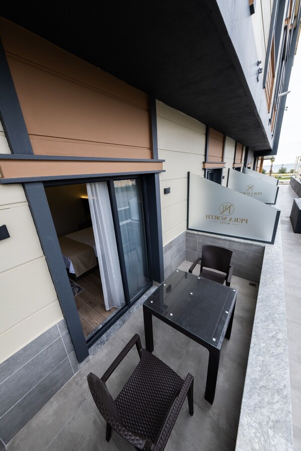 Een terras met glazen scheiding, een bed zichtbaar door de scheiding, en een bord met de naam van het hotel.