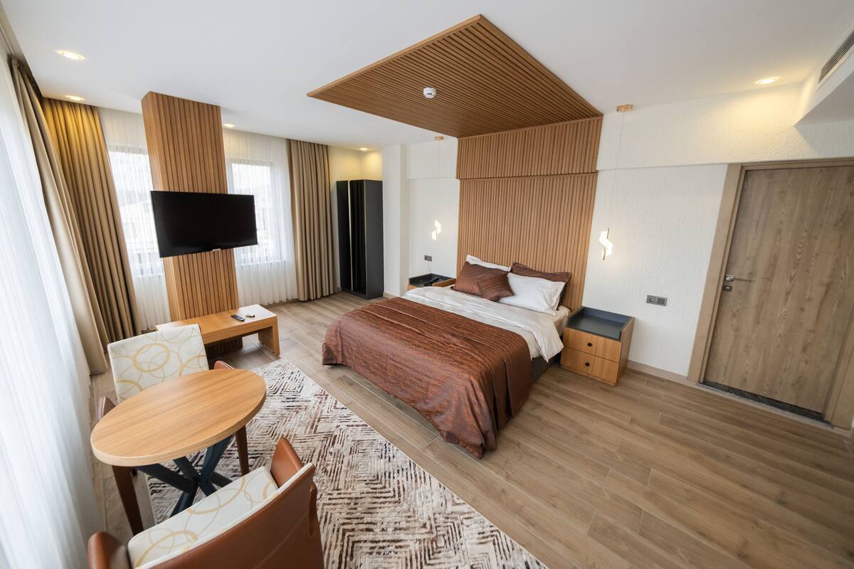Une chambre d’hôtel moderne dotée d’un grand lit, d’un téléviseur fixé au mur, d’un plafond en bois et d’un bureau avec une chaise.