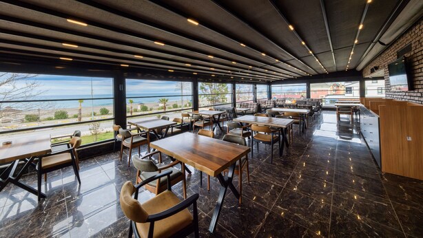 A modern restaurant with a view of the sea, featuring wooden tables and chairs, a brick wall, and a high ceiling with exposed beams.