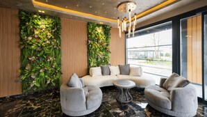 A modern lobby with a curved sofa, two armchairs, a round coffee table, and a large window offering a view.