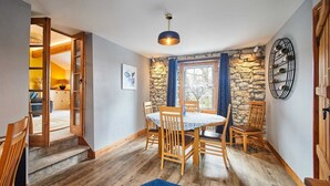 A dining area with a round table, wooden chairs, a blue rug, and a stone wall.