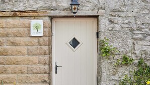 A door with a small window, a wall-mounted light fixture, and a sign with a tree illustration.