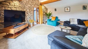 A cozy living room with a stone wall, wooden entertainment unit, and comfortable seating including a blue armchair and a dark sofa.