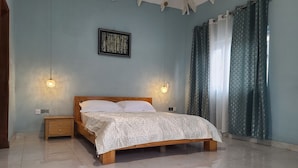 Une chambre à coucher avec un lit en bois, deux tables de chevet, une lampe fixée au mur et une fenêtre avec des rideaux.