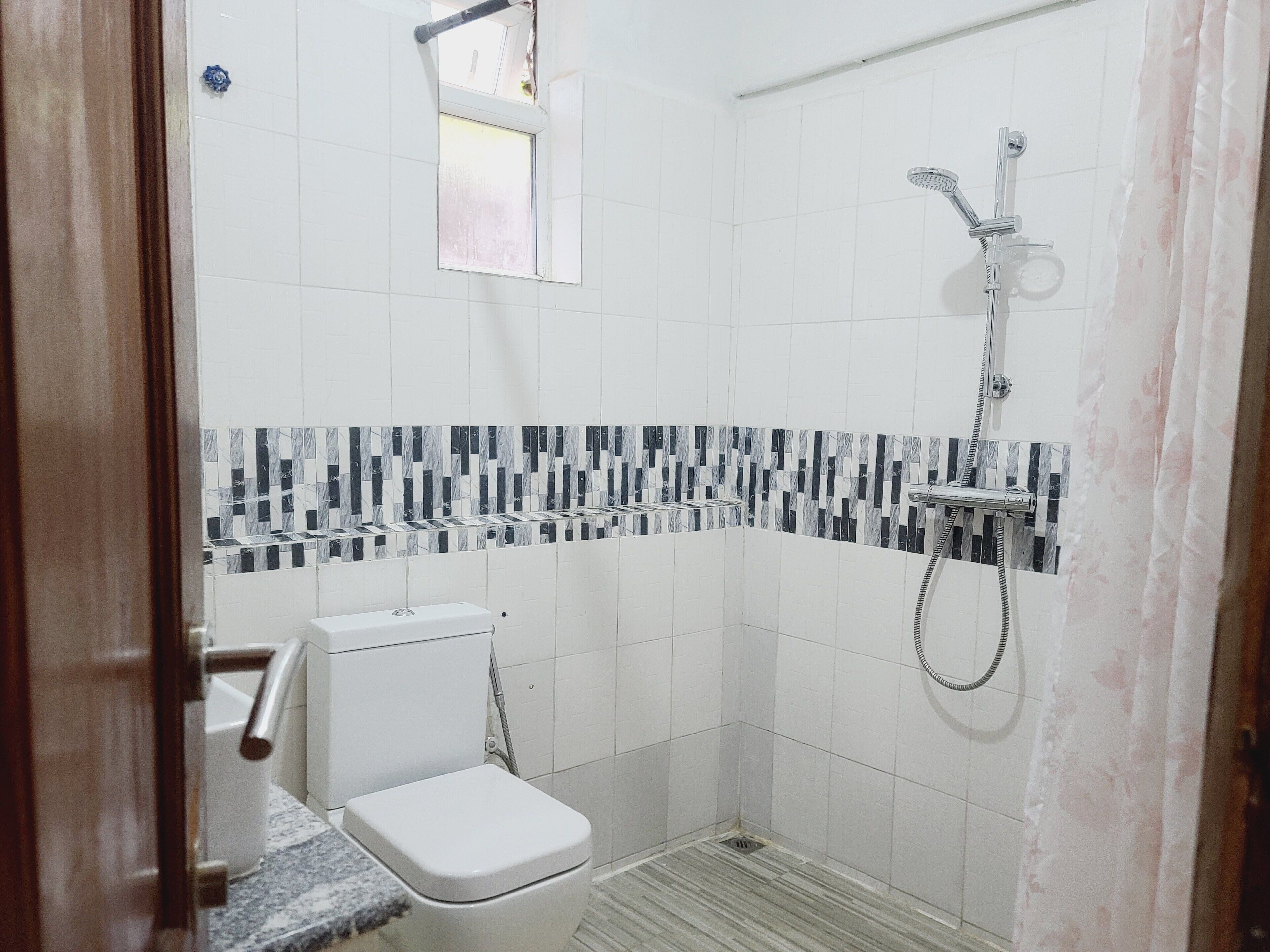 A small, tiled bathroom with a shower, toilet, and a window.
