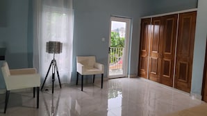 Une pièce avec un fauteuil blanc, un lampadaire sur trépied, une armoire en bois et une porte donnant sur un balcon.