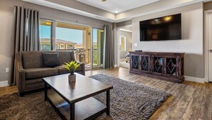 A modern living room with a sofa, coffee table, and a flat-screen TV mounted on the wall. - Sunset Point: 3 bedroom, 3 baths, 3rd Floor Condo.  Pool and Hot Tub. (St. George)