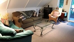 Un salon chaleureux de style industriel, avec un plafond haut, une table basse en verre, un canapé, un fauteuil et une cheminée.