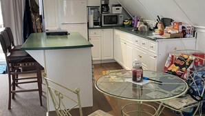 Une cuisine compacte avec un coin repas, comprenant un petit îlot, des meubles blancs, un four à micro-ondes et une table en verre avec des chaises.