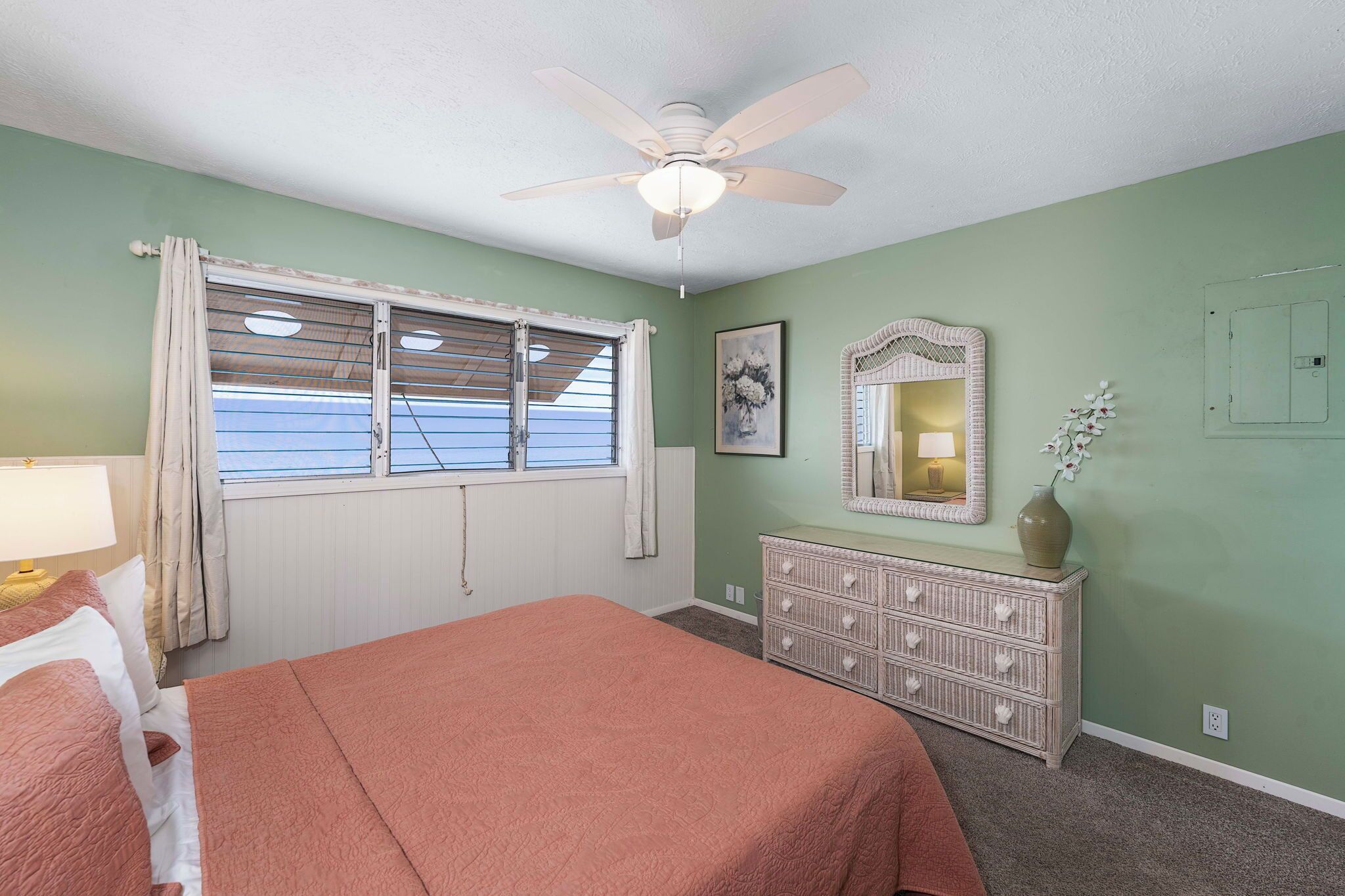 A bedroom with a bed, a dresser, a ceiling fan, a window with blinds, and a wall-mounted mirror.