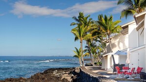 Une propriété située en bord de mer, dotée d’une terrasse avec des chaises rouges et une table, et offrant une vue sur l’océan.