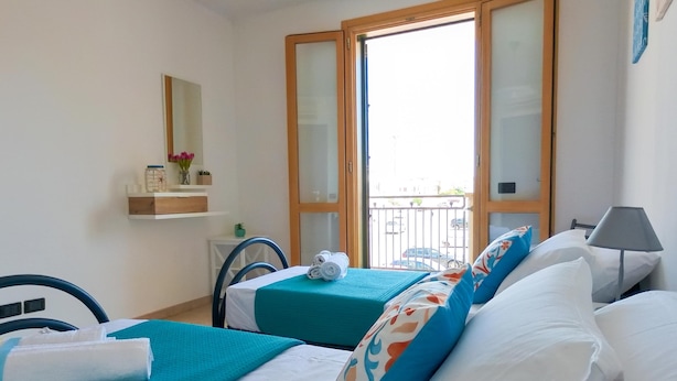 Een hotelkamer met twee bedden, een tafeltje, een stoel, een raam met uitzicht op de straat, en een plank met decoratieve objecten.